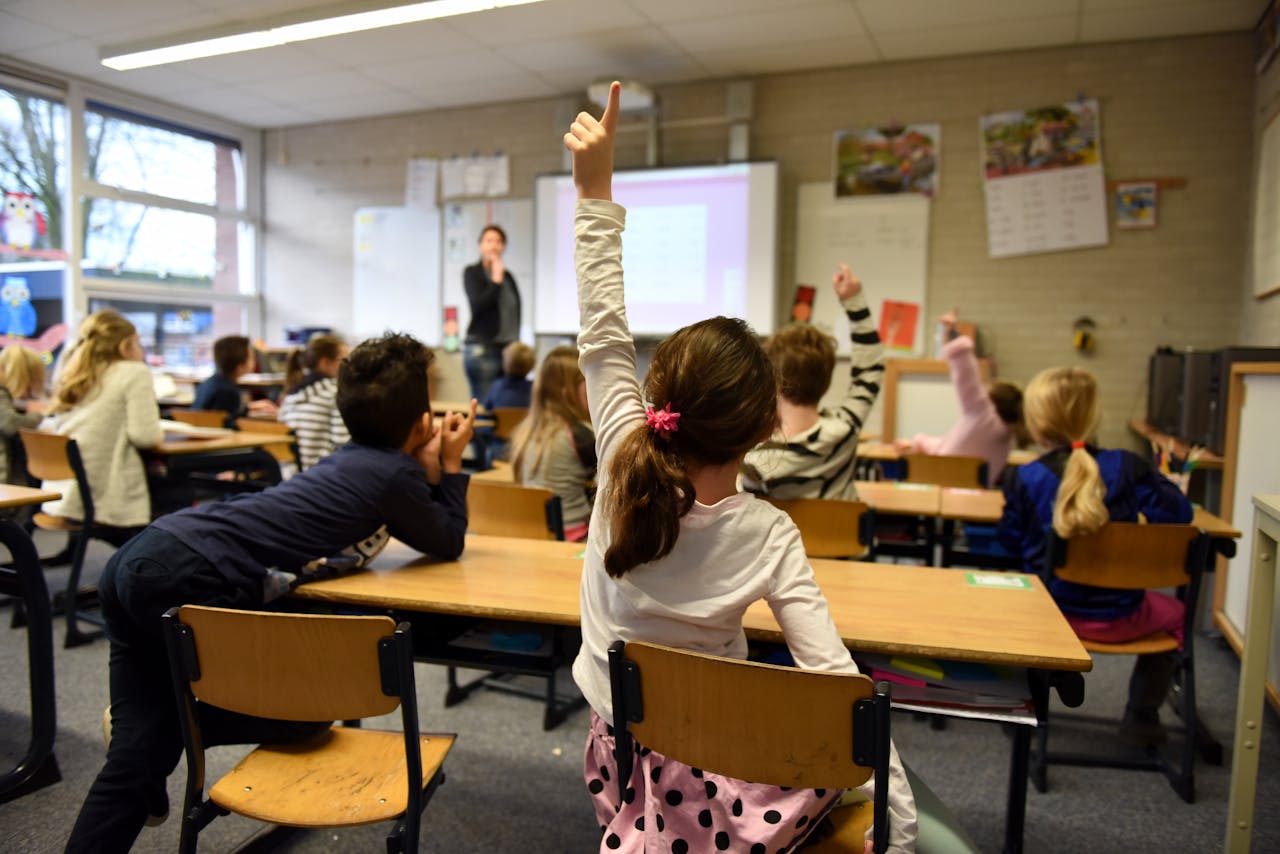 about-us-02 Lively classroom scene with students participating actively, raising hands for a lesson.